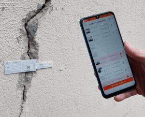 Saugnac app on a smartphone reading a G1 crack gauge fitted on a wall